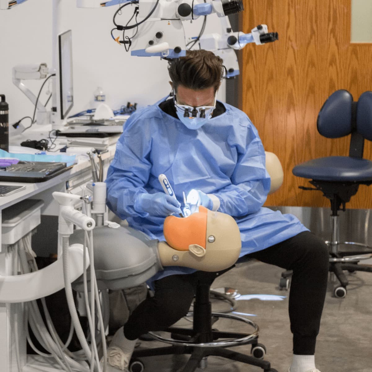A participant working directly on the manikin with loupes pushed up on the forehead, instrument and mirror in hand and rubber dam placed